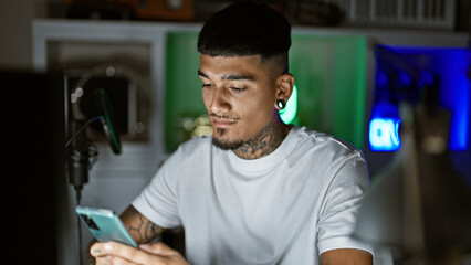 Handsome young latin man, tattooed musician, emotively expressing his song on smartphone amidst the...