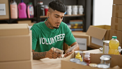 Young handsome tattooed latin man counting donation dollars as a volunteer at a charity center, portraying altruism in his community