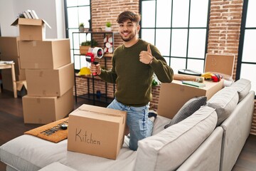 Arab man with beard moving to a new home closing cardboard box smiling happy and positive, thumb up...
