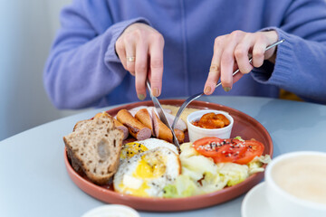 Obraz na płótnie Canvas Woman eating healthy morning meal. Healthy breakfast with eggs, sausages, lettuce, tomatoes, beans, butter, freshly baked bread
