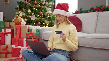Obraz na płótnie Canvas Young blonde woman shopping with laptop and credit card sitting on floor by christmas tree at home