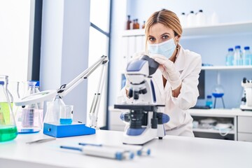 Naklejka na ściany i meble Young blonde woman scientist wearing medical mask using microscope at laboratory