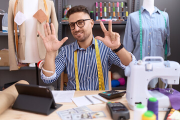 Hispanic man with beard dressmaker designer working at atelier showing and pointing up with fingers number eight while smiling confident and happy.