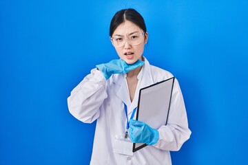 Chinese young woman working at scientist laboratory cutting throat with hand as knife, threaten aggression with furious violence