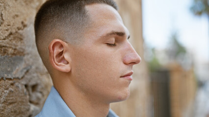 Handsome young hispanic man in casual attire standing on a city street with eyes closed and serene expression.