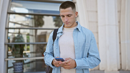 A handsome young hispanic man checking his smartphone on a sunny urban campus street.