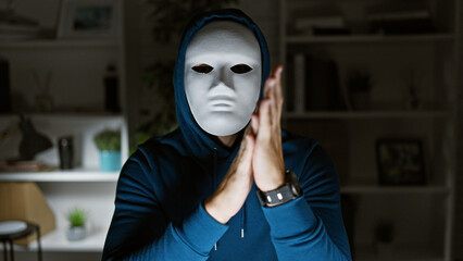 A mysterious person in a mask applauds silently in a dimly lit modern office space.