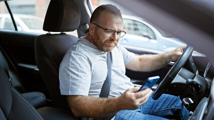 Handsome middle-aged caucasian man sitting in his car, smiling confidently as he types a message on...