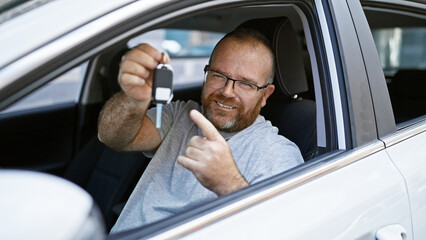 Handsome, bearded, middle-aged caucasian man, smiling confidently, pointing to the key of his new car on a sunny city street- pure enjoyment.