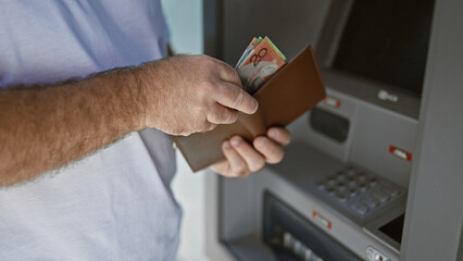 Handsome middle-aged caucasian man outside on urban street, captivating portrait of him holding wallet counting australian cash dollars at atm machine, engaging in banking transaction.