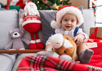 Fototapeta na wymiar Adorable caucasian baby holding horse toy sitting on sofa by christmas tree at home