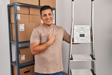 Hispanic young man working at small business ecommerce holding ladders smiling happy pointing with...