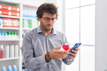 Young hispanic man customer using smartphone holding medicine bottle at pharmacy