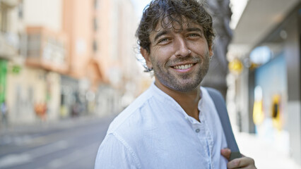 Handsome hispanic man with green eyes and beard smiling on a sunny urban street.