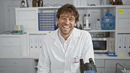 Handsome bearded hispanic man in white lab coat smiling in a modern laboratory setting