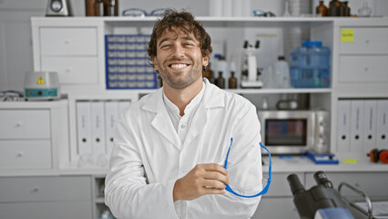 Naklejka na ściany i meble Smiling hispanic man with beard wearing lab coat in a modern laboratory environment