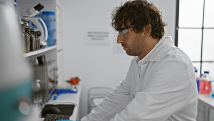 Fototapeta na wymiar A focused man in safety glasses works meticulously in a modern laboratory with scientific equipment.