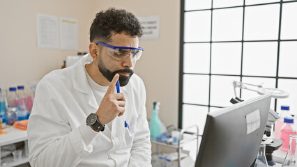 Naklejka na ściany i meble Thoughtful hispanic man wearing glasses and lab coat contemplating in a science laboratory.