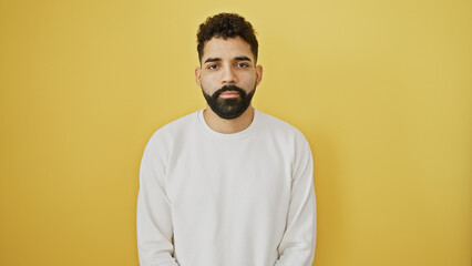 A handsome young man with a beard stands against a solid yellow background, exuding casual...