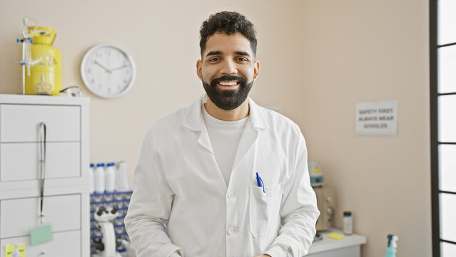 Handsome hispanic man with beard wearing a lab coat standing in a bright hospital room