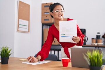 Young chinese woman business worker reading document writing on paperwork at office