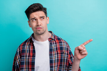 Photo of doubtful unsure man dressed plaid shirt looking pointing finger empty space isolated...