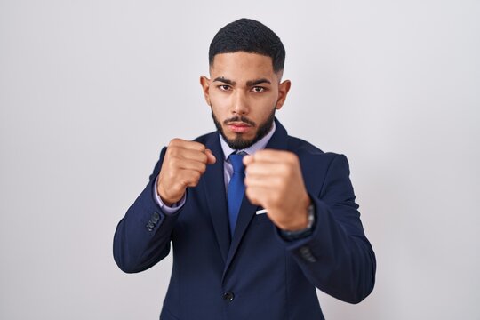 Young hispanic man wearing business suit and tie ready to fight with fist defense gesture, angry and upset face, afraid of problem