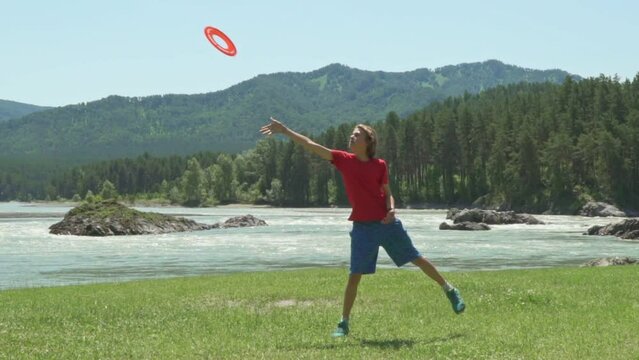 Slow motion. Young Boy throwing a red frisbee disk.  Young boy playing on a mountain river bank. Cute boy playing with frisbee 