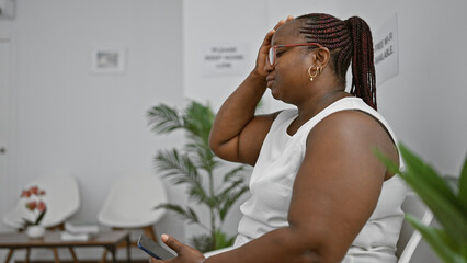 Stressed african american woman, a successful manager, sitting tensely in chair of waiting room,...