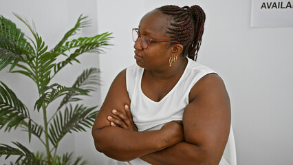 Serious african american woman, a successful manager with braids and glasses, sits relaxed yet...