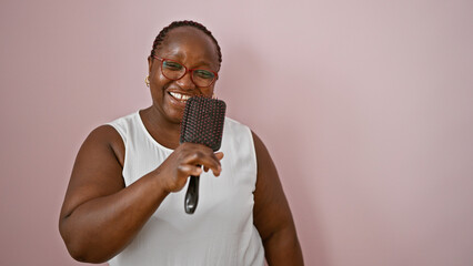 Confident, happy african american woman letting loose; singing her heart out, dancing using brush as mic over pink isolated background! enjoy the music, the voice and smile!!