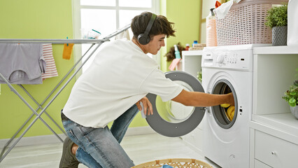 Handsome young hispanic teenager rocks out, engrossed in music, while tackling laundry chores in...