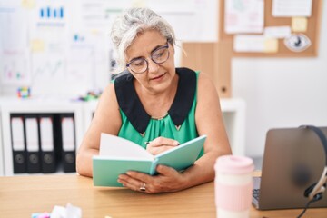 Middle age grey-haired woman business worker reading book at office
