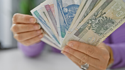 A mature woman counts various polish zloty banknotes in a bright office setting.