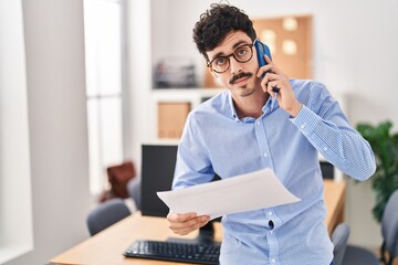 Young caucasian man business worker talking on smartphone reading document at office