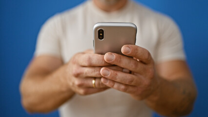 Handsome young man with beard using smartphone against blue backdrop, portraying connectivity and modern lifestyle.