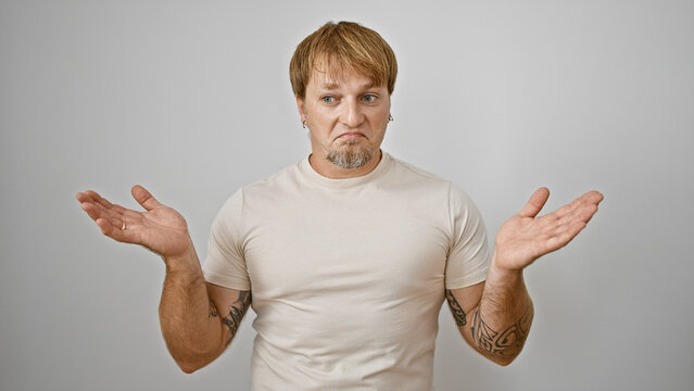 Perplexed young adult caucasian man with beard and tattoos gesturing uncertainty against a white background.