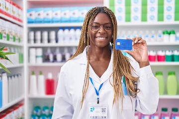 African american woman with braided hair working at pharmacy drugstore holding credit card looking...