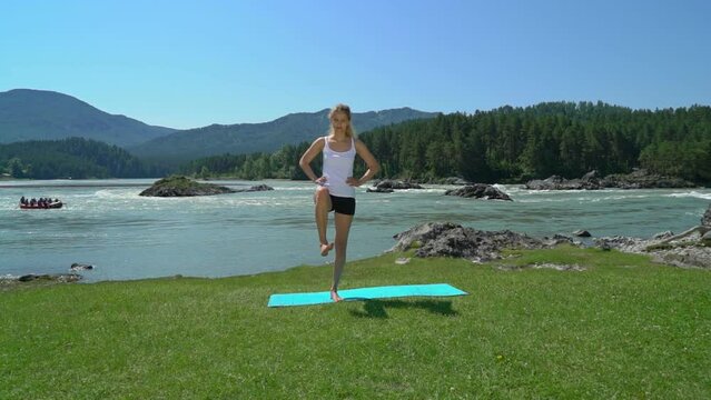 Young woman does yoga against mountain and mountain river view. 
Girl doing complex Yoga exercise headstand with Namaste asana. Amazing Yoga landscape in beautiful mountains.