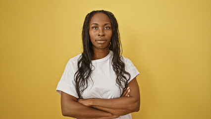 Confident adult woman with crossed arms against a vibrant yellow background, presenting a portrait...