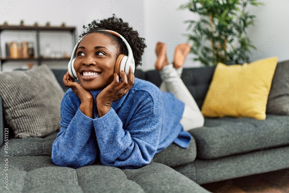 Wall mural african american woman listening to music lying on sofa at home