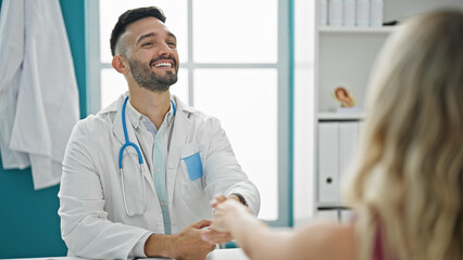 Young hispanic man doctor shaking hands with patient at the clinic