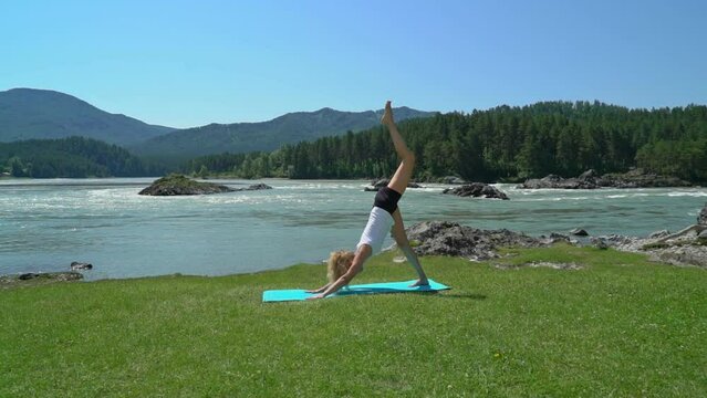 Young woman does yoga against mountain and mountain river view. 
Girl doing complex Yoga exercise headstand with Namaste asana. Amazing Yoga landscape in beautiful mountains.