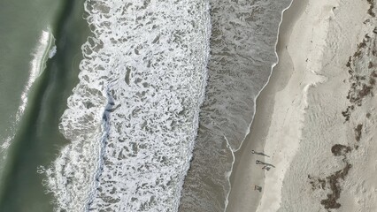 Drone view looking down on ocean beach coastline with waves and sunlight in early morning of day