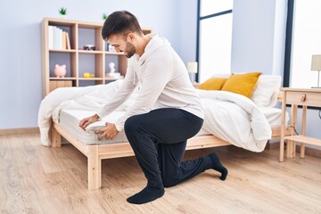 Fototapeta premium Young hispanic man smiling confident touching mattress at bedroom