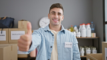 Handsome young hispanic man happily volunteering at a charity center, confidently flashing thumb up...