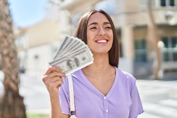 Young beautiful hispanic woman smiling confident holding dollars at street