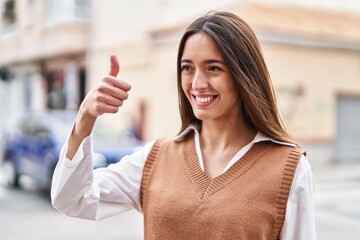 Young beautiful hispanic woman smiling confident doing ok sign with thumb up at street