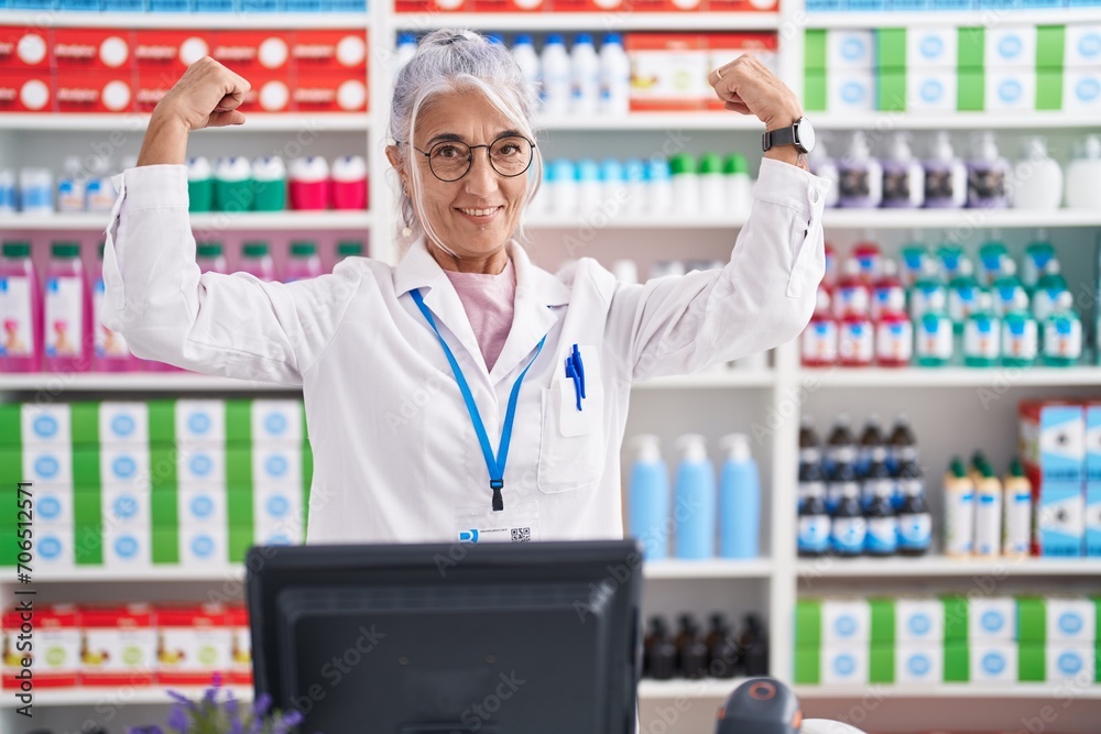 Poster middle age woman with tattoos working at pharmacy drugstore showing arms muscles smiling proud. fitn