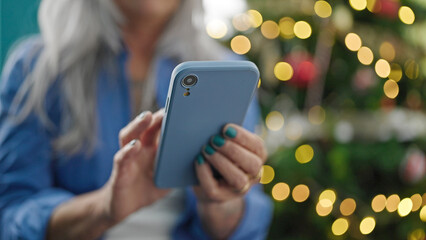 Middle age grey-haired woman using smartphone celebrating christmas at home